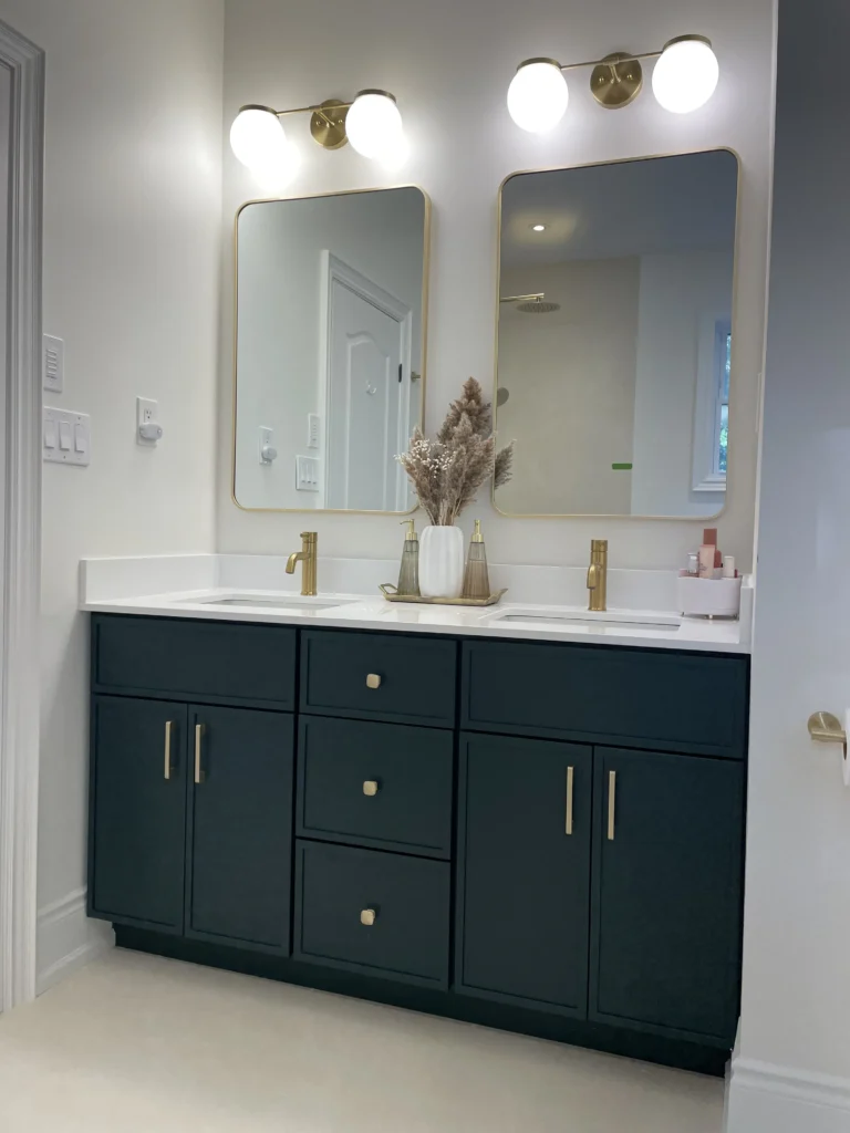 Modern double-sink bathroom vanity with black cabinets, brass fixtures, and decorative vases.